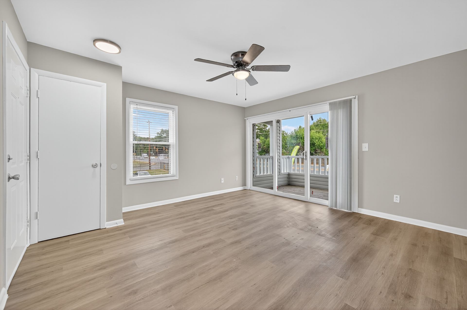 Empty gray bedroom with wood floors, ceiling fan, and sliding glass doors to a balcony.