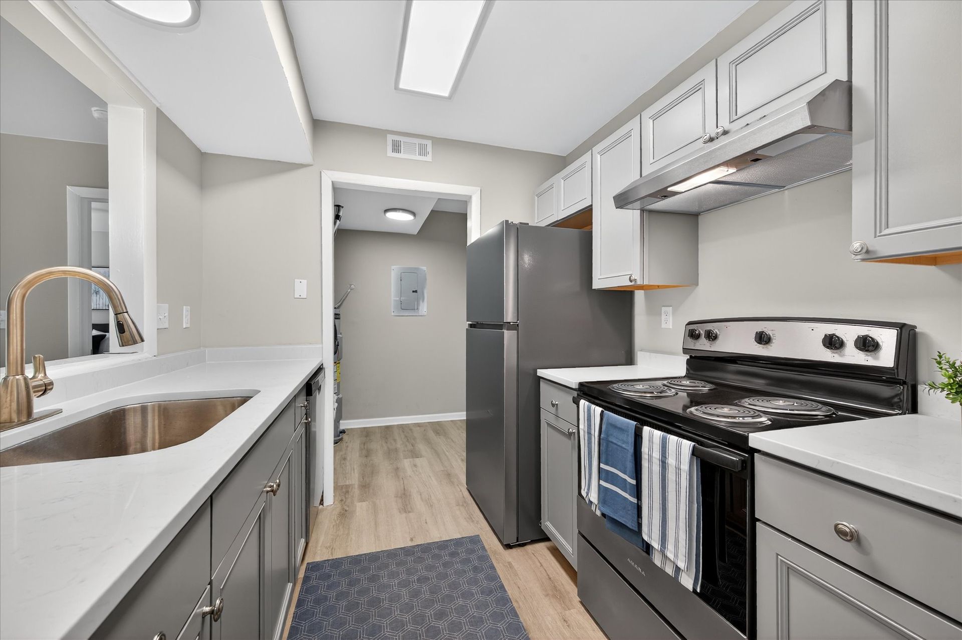 Bright galley kitchen with white cabinets, stainless appliances, gray counters, and a light wood floor.