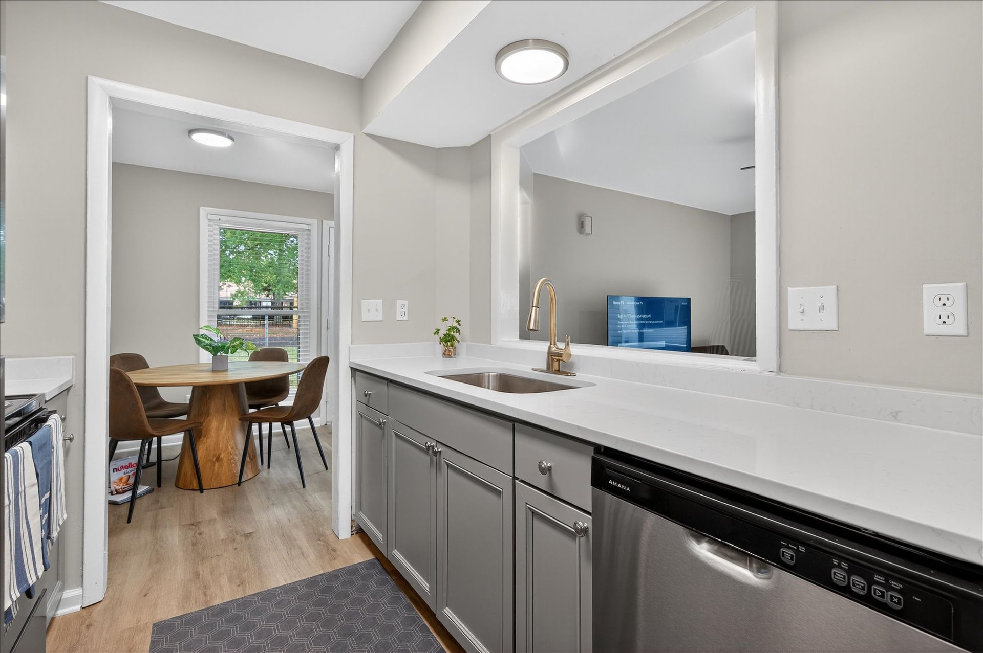 Bright kitchen vanity with white countertop, gray cabinets, and dining area visible through doorway.