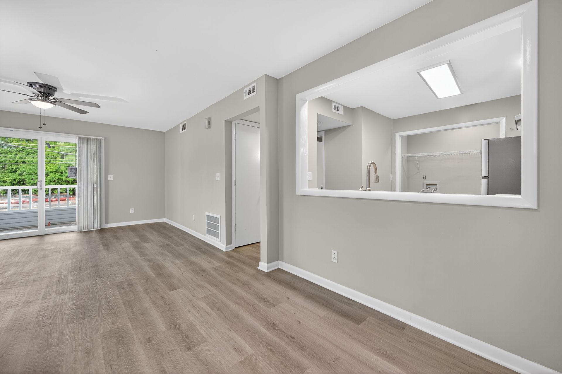 Empty modern living room with gray walls, wood floors, and an open pass-through to a kitchen.