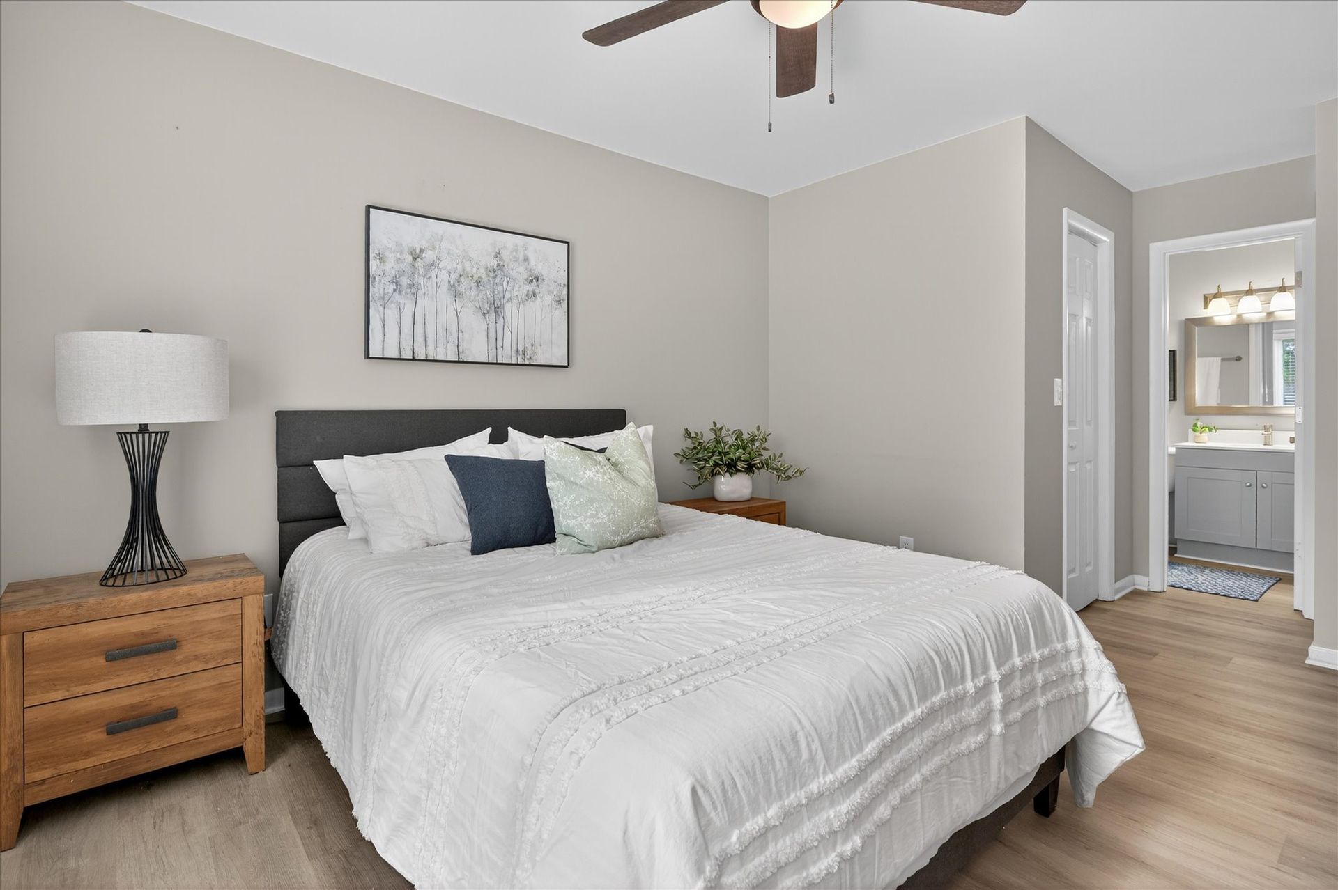 Bright bedroom with a white bed, wooden nightstands, ceiling fan, and hallway entrance
