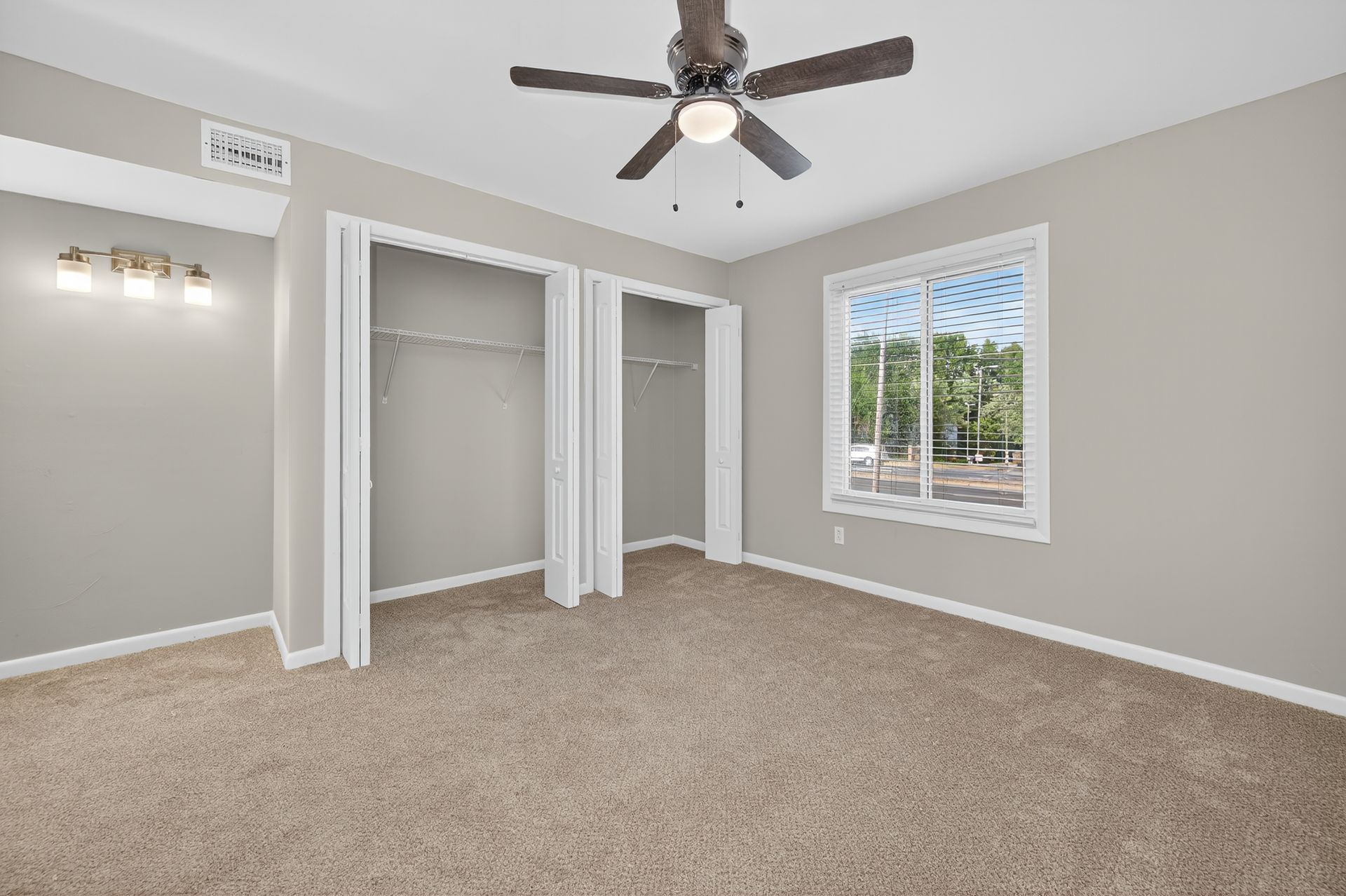 Empty beige bedroom with carpet, ceiling fan, open closet, and window with white blinds