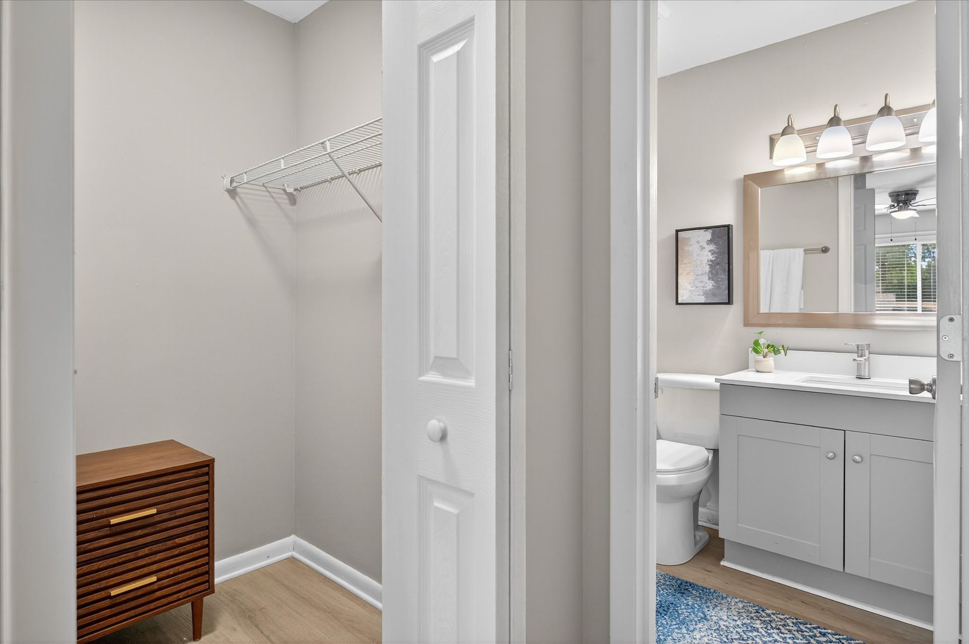 Small closet beside a bathroom vanity with wicker hamper, white walls, and light wood flooring