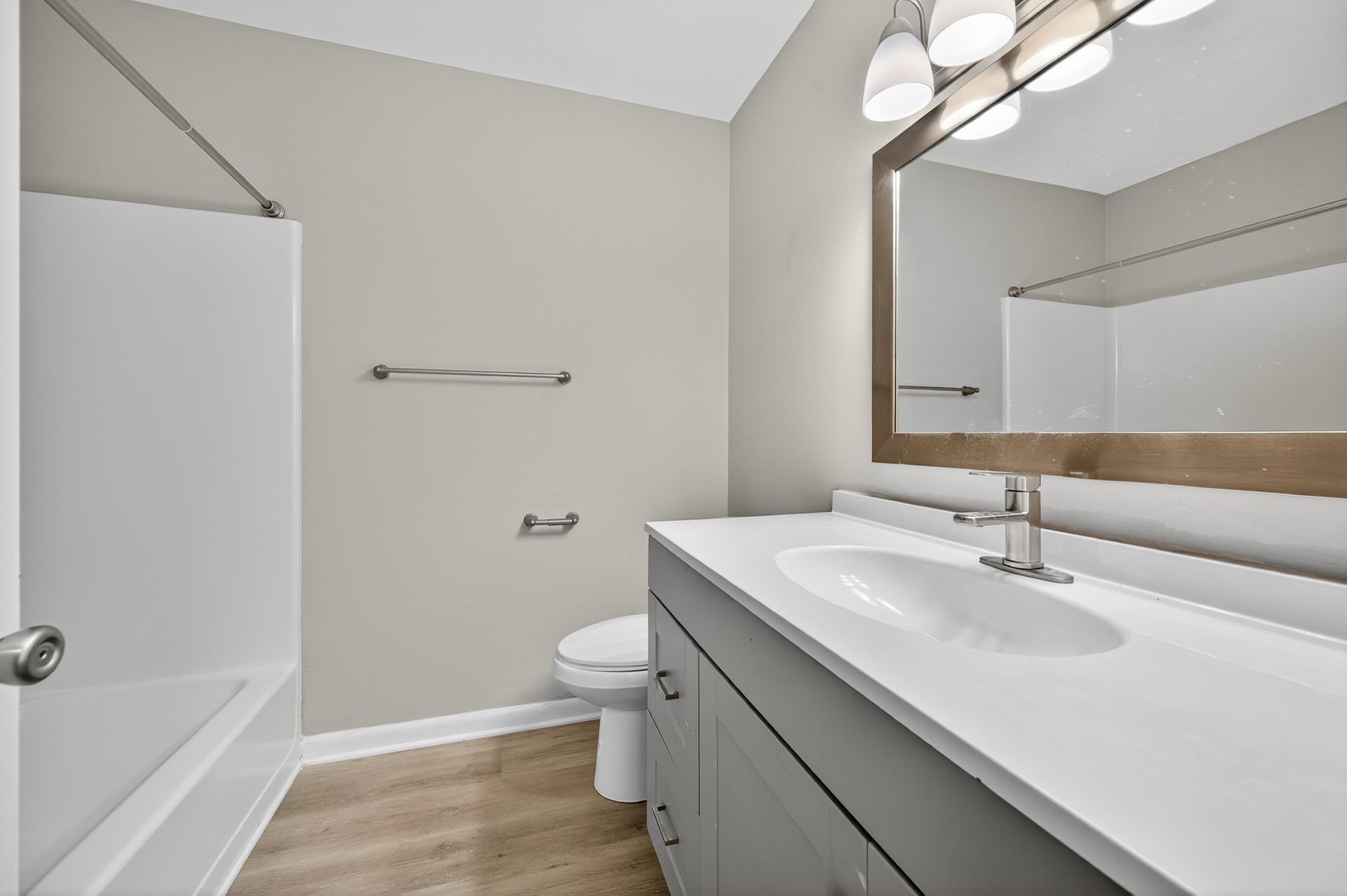 Modern bathroom with white vanity, large mirror, tub, toilet, and gray walls