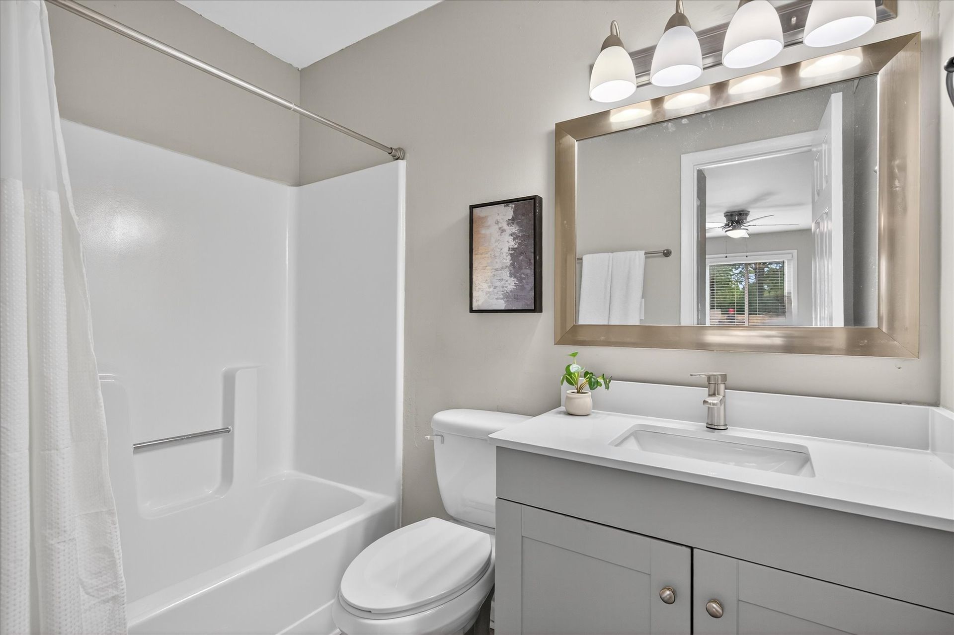 Bright bathroom with white tub, gray vanity, large mirror, and modern light fixture