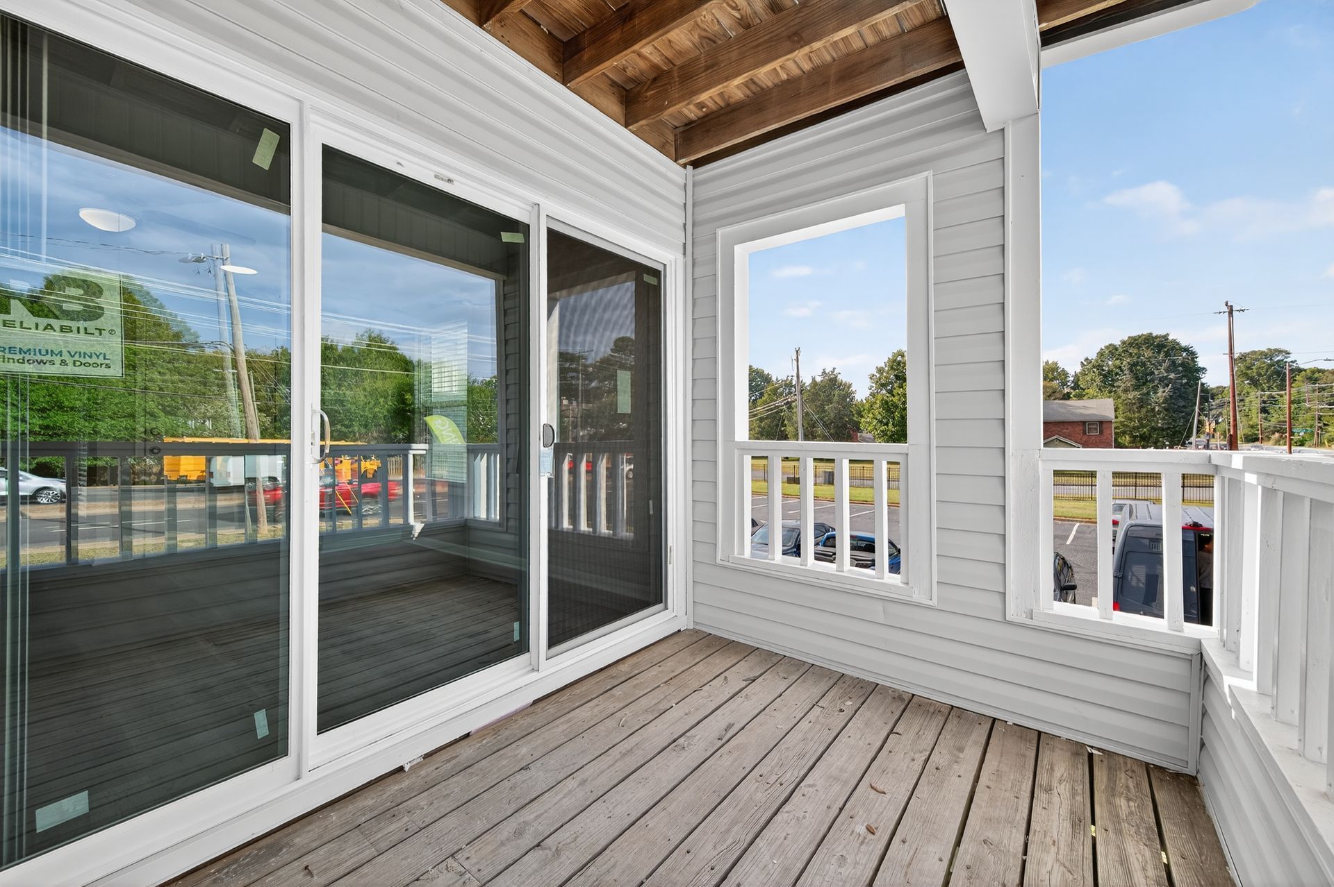 Covered balcony with wood floor, sliding glass door, and white railing overlooking a street.