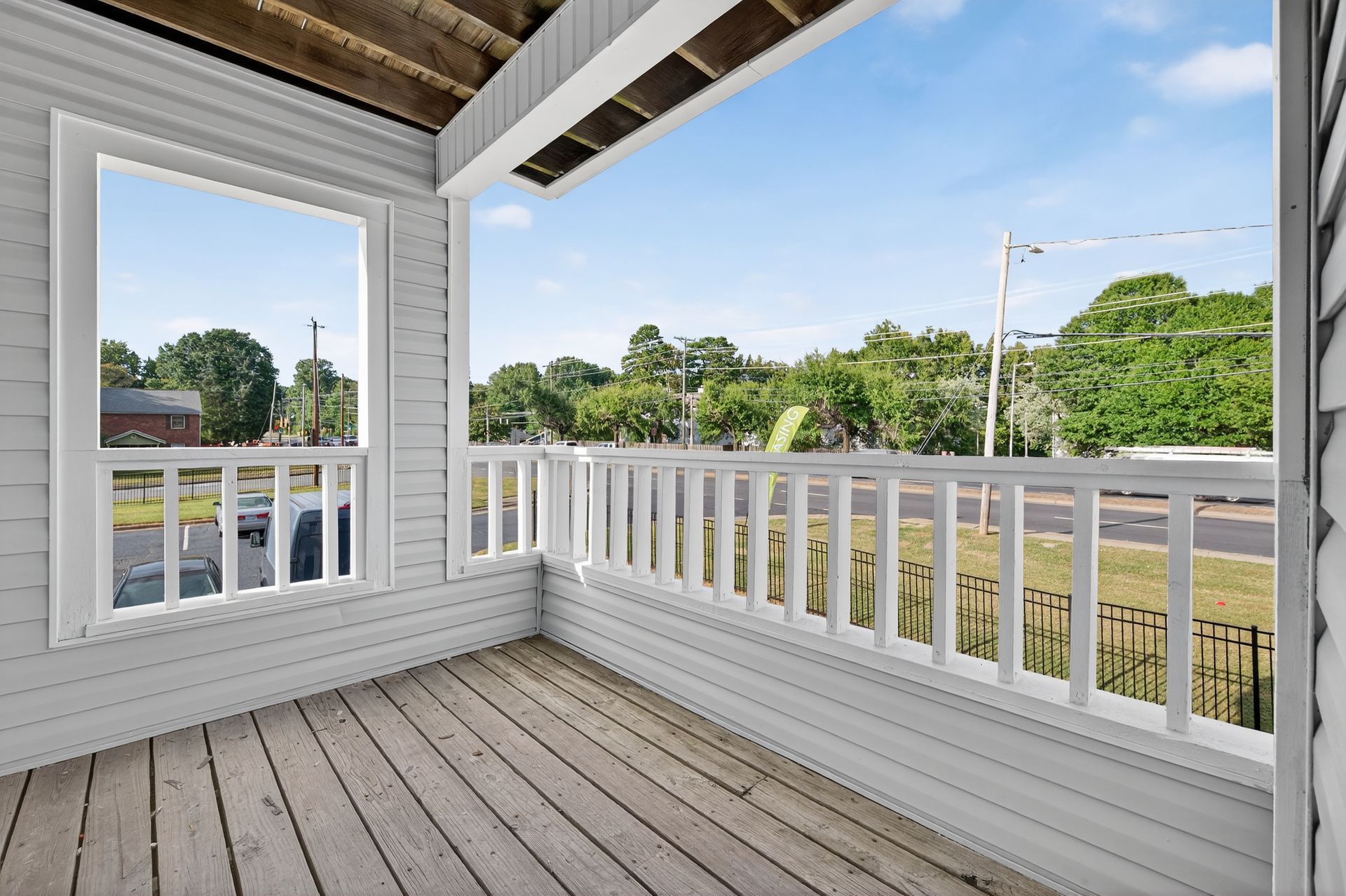 Covered porch with white railings and a view of trees and a road beyond.