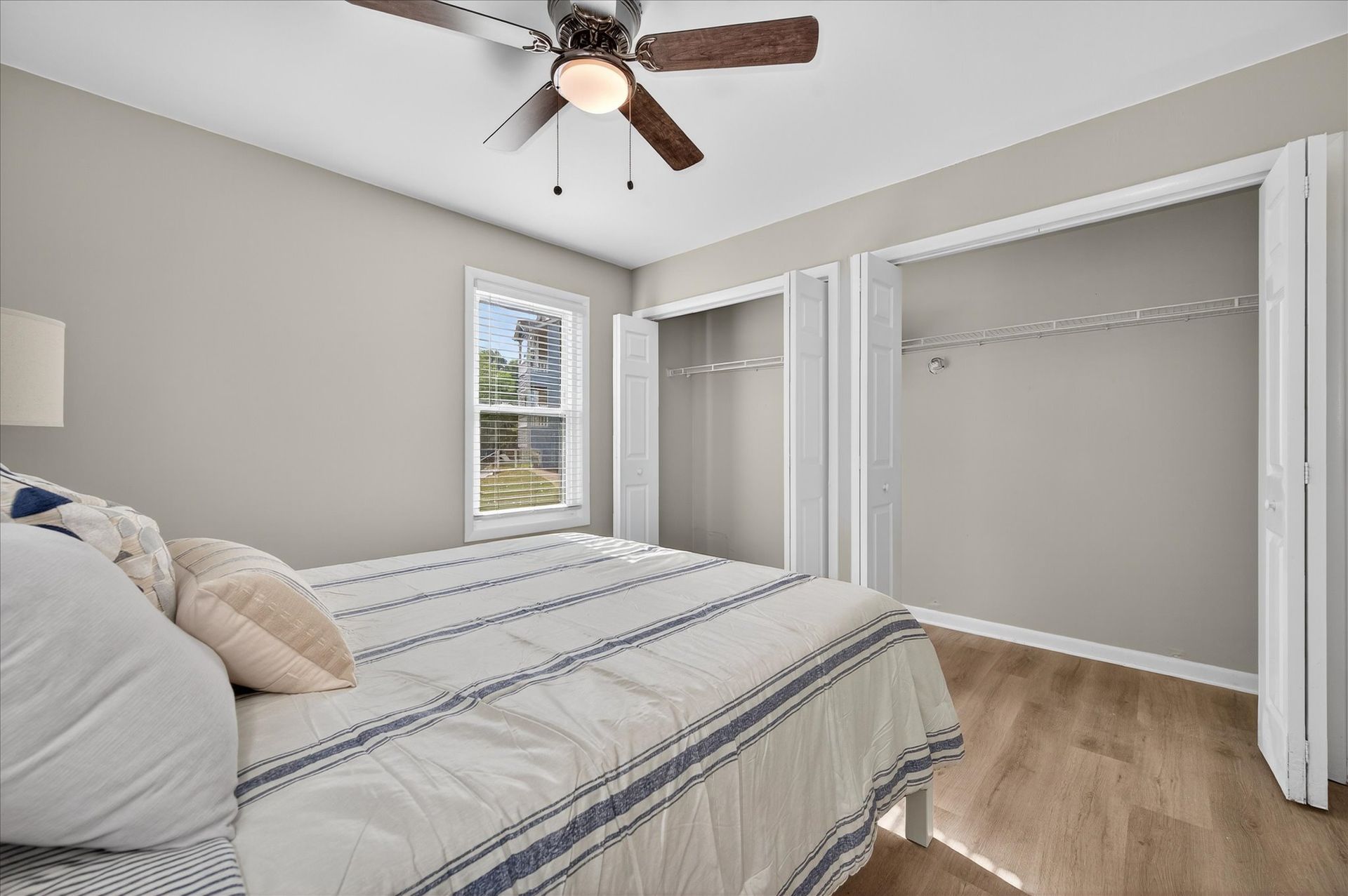 Bright bedroom with striped bedspread, open closet, window, and ceiling fan