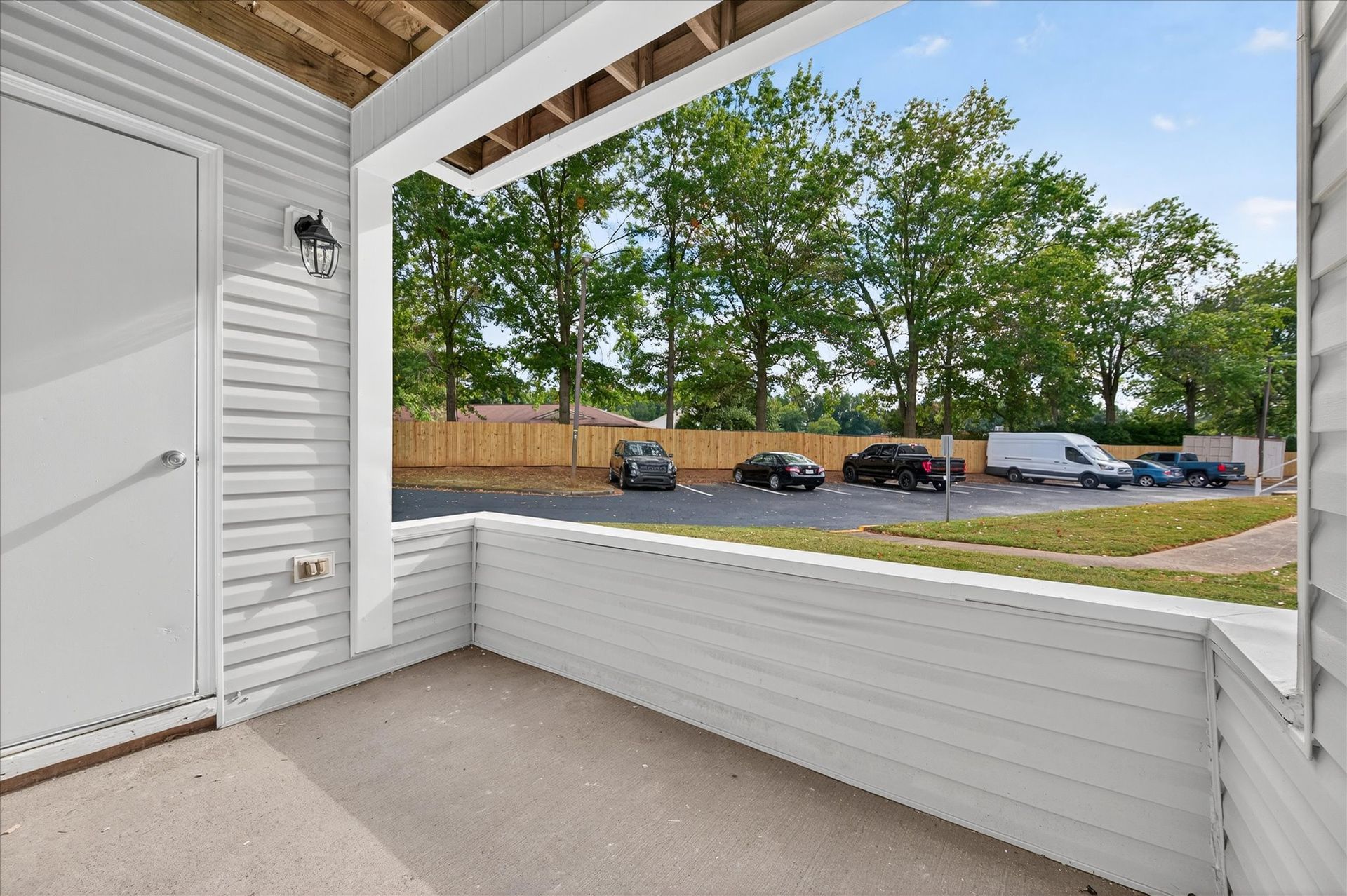 Covered front porch overlooking parking lot and trees, with white siding and a railing.