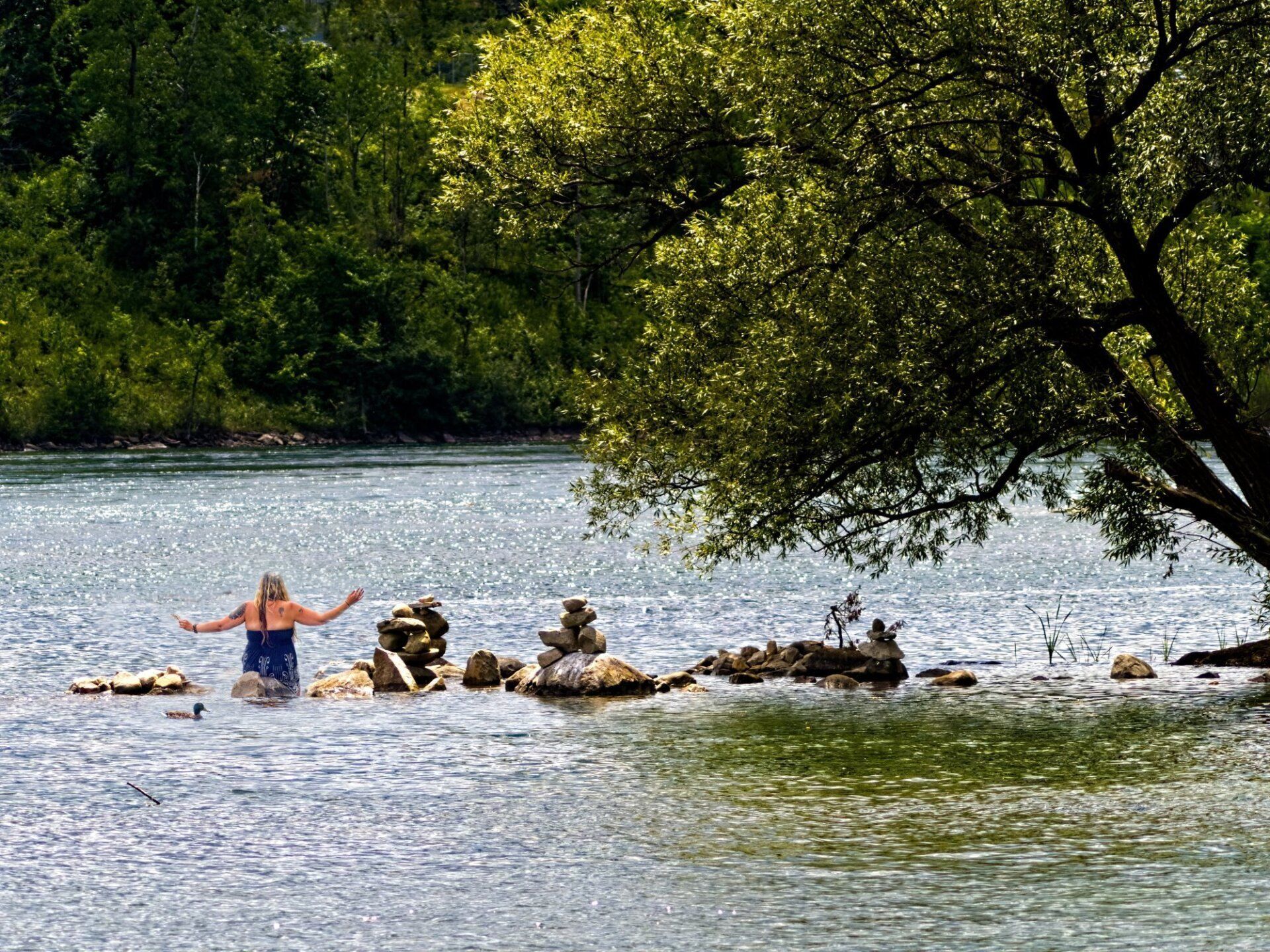 Une femme se tient debout sur un rocher au milieu d'une rivière.
