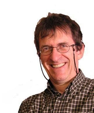 Un homme portant des lunettes et des écouteurs sourit à la caméra