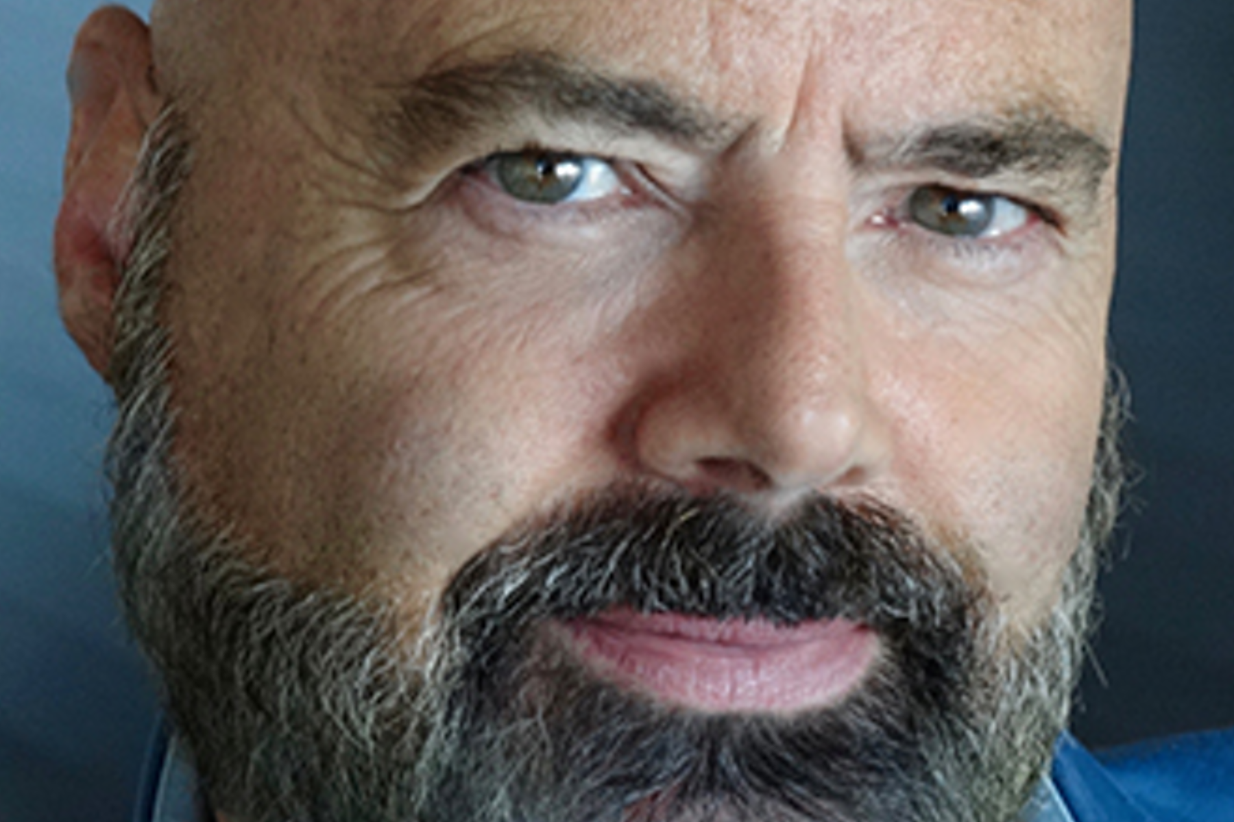 Un homme avec une barbe et une moustache regarde la caméra.
