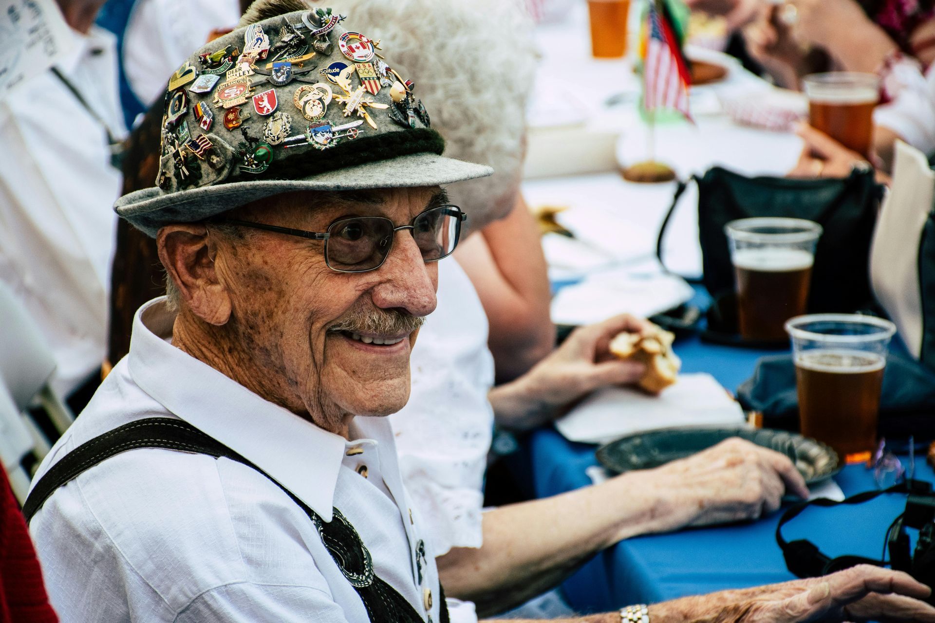 An elderly man wearing a hat and sunglasses is sitting at a table.