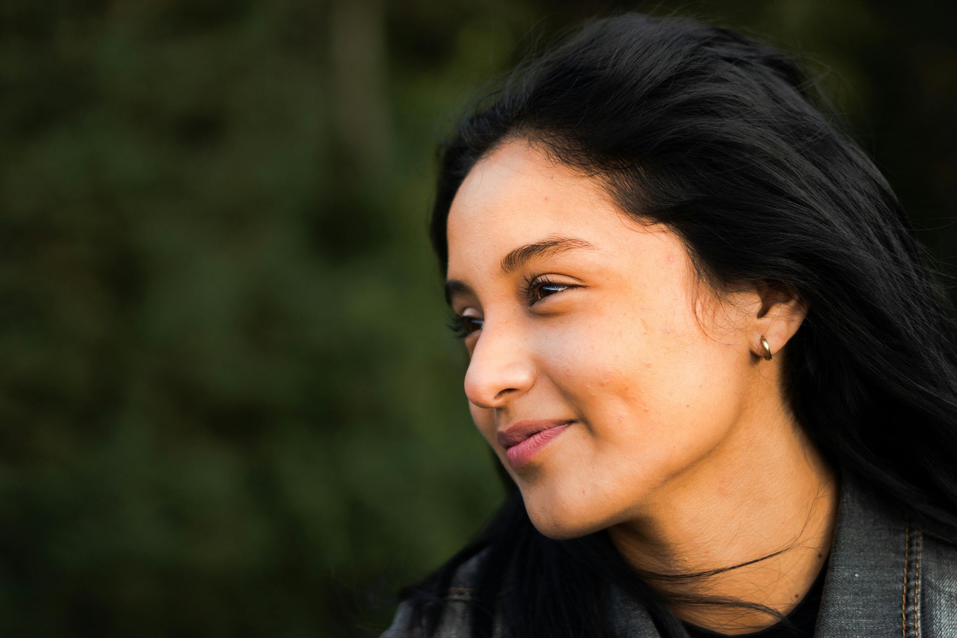 A woman with long black hair is smiling and looking to the side.