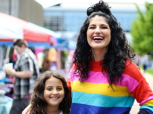 A woman in a rainbow sweater is standing next to a little girl.