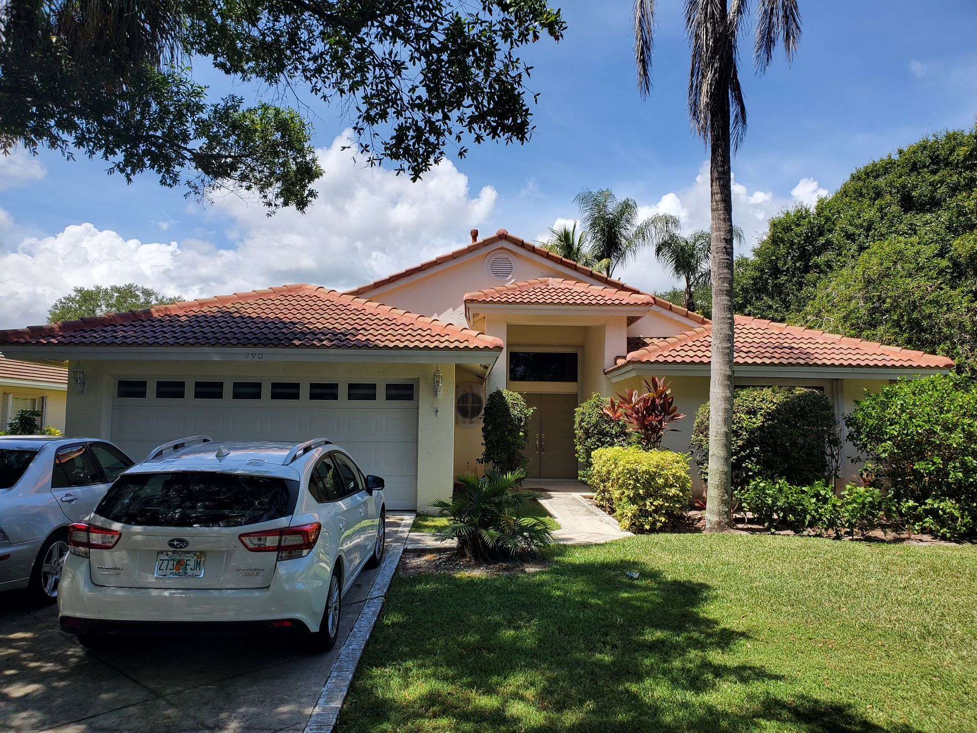 A white car is parked in front of a large house.