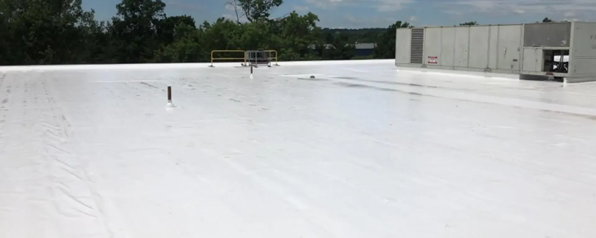 A white roof with a building in the background and trees in the background.