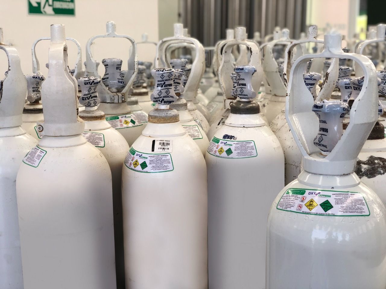 Filas de bombonas de gas blanco con válvulas en una zona de almacenamiento industrial.