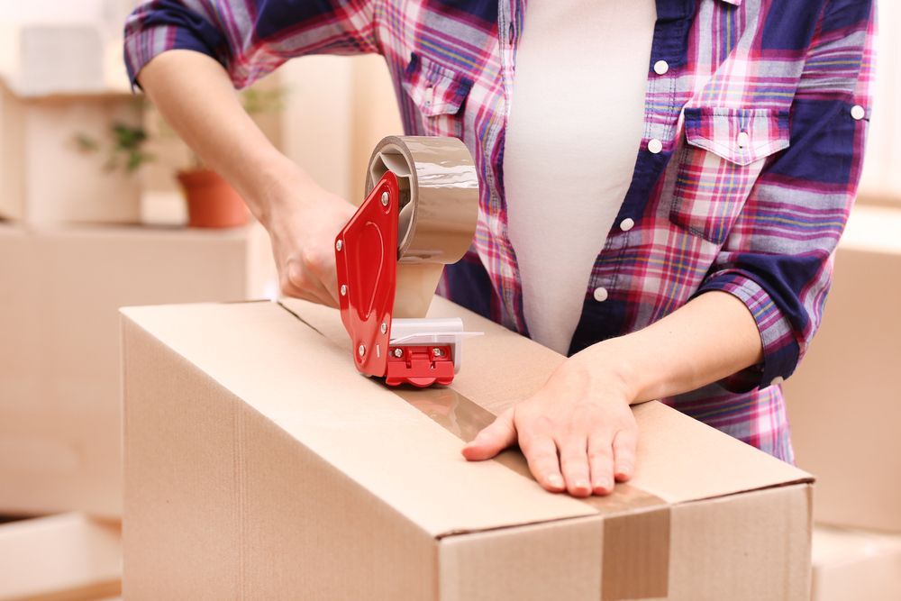 Woman Taping a Cardboard Box Shut with A Red Tape Dispenser — Barnes Transport and Removals in Byron Bay, NSW