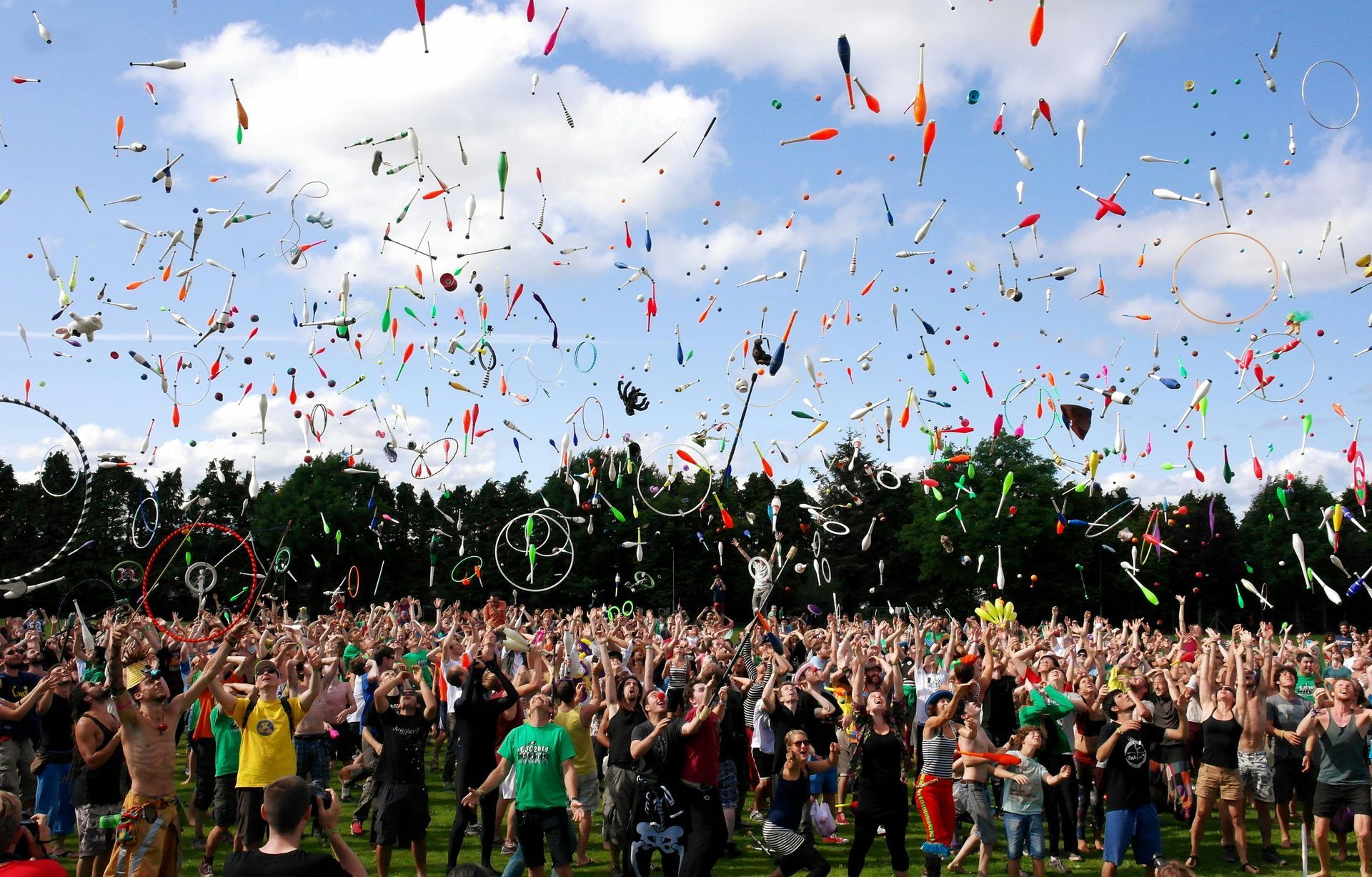 Gran multitud con los brazos en alto bajo un cielo lleno de serpentinas y confeti de colores, en un campo verde.