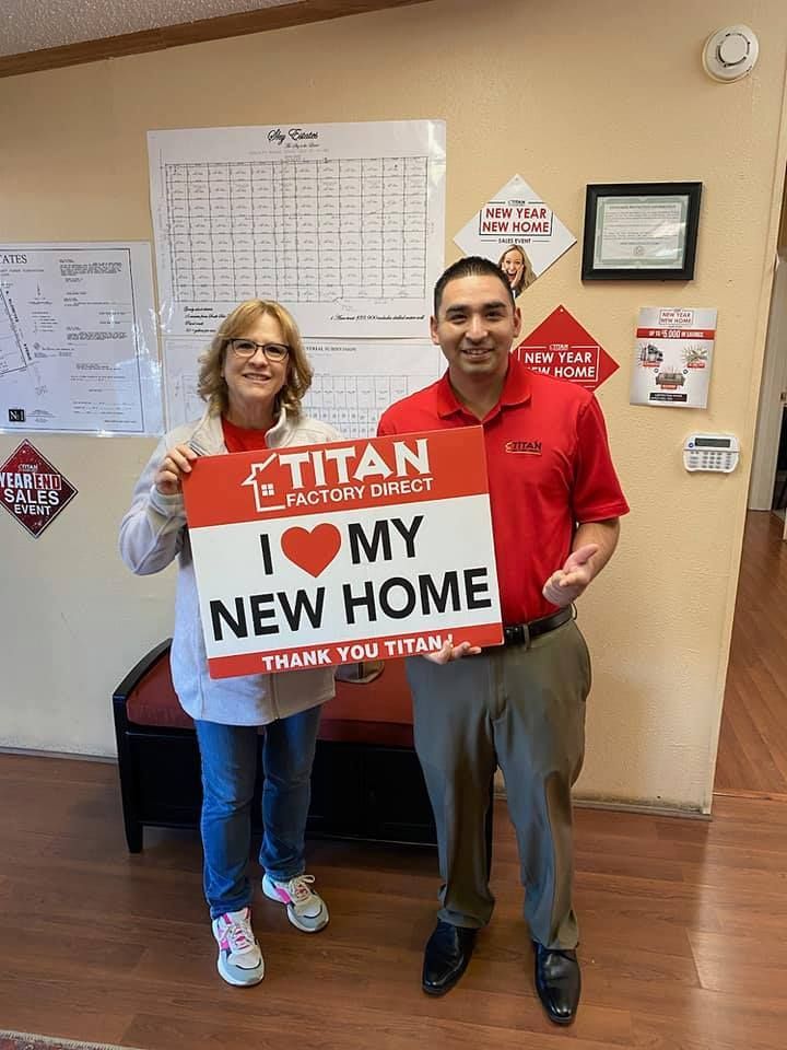 Two people in an office holding a red sign reading “I ♥ MY NEW HOME” and “TITAN”