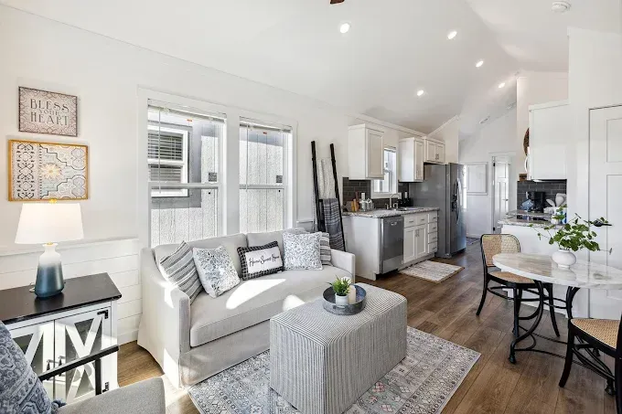 Bright modern living room and kitchen with gray sofa, dining nook, and light wood floors