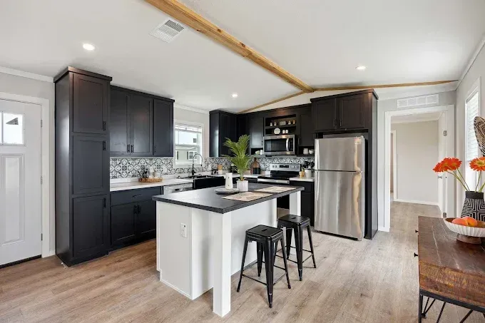 Modern kitchen with dark cabinets, stainless fridge, white island, and two stools