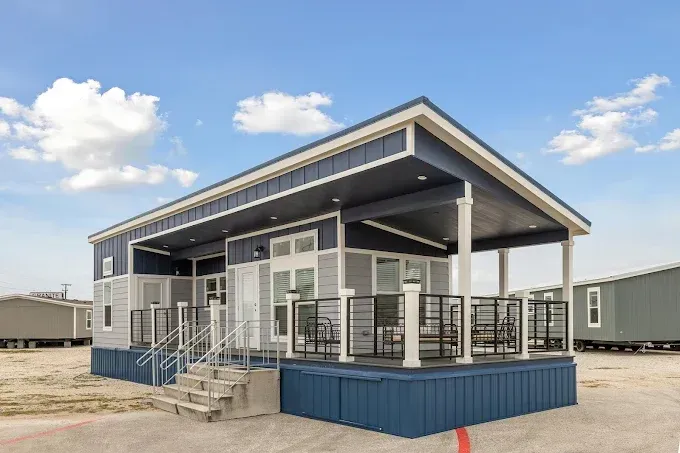 Modern portable building with blue trim, covered porch, and steps in an open industrial yard under a cloudy sky