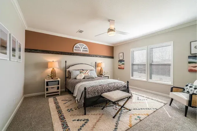 Bright bedroom with a bed, bench, bedside table, window shutters, and neutral decor