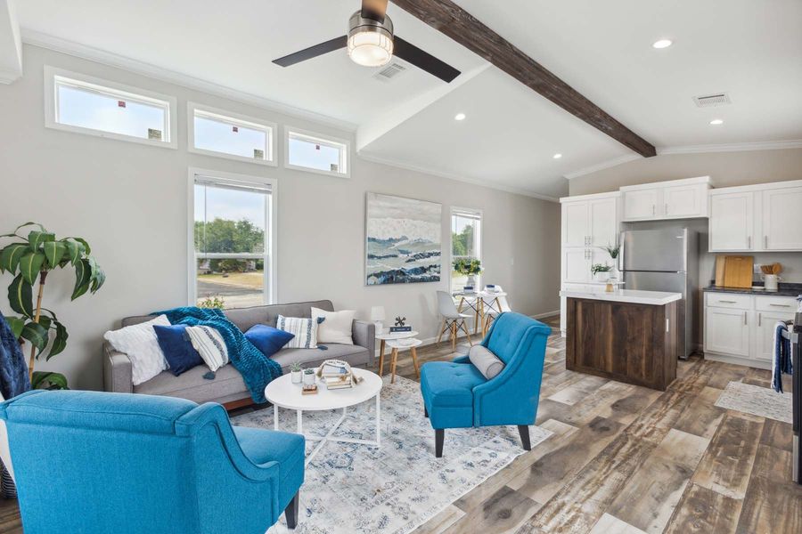 Bright living room with blue chairs, gray sofa, vaulted ceiling, and open kitchen with wood accents.