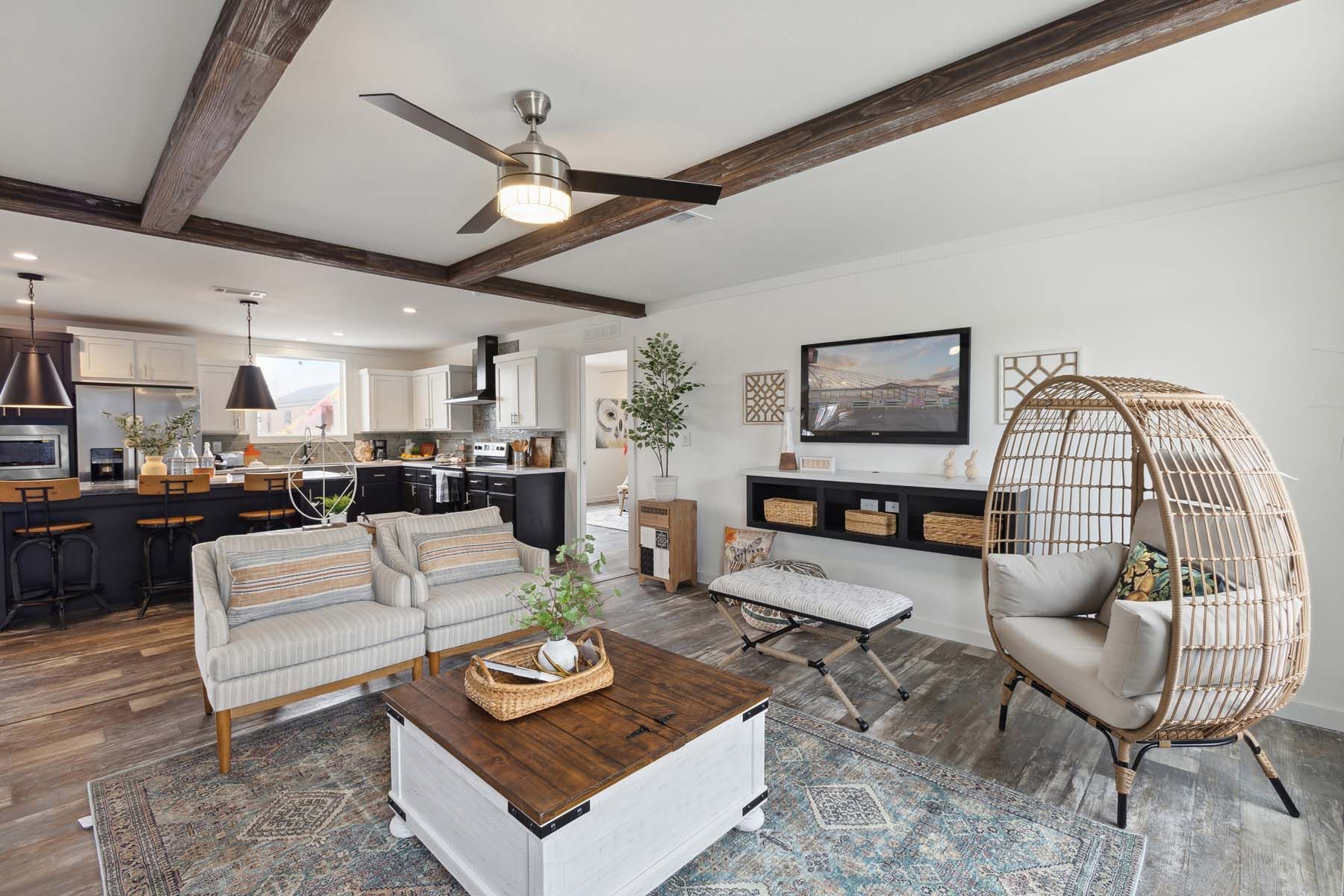 Stylish open living room with sectional, wicker chair, coffee table, TV, and exposed ceiling beams