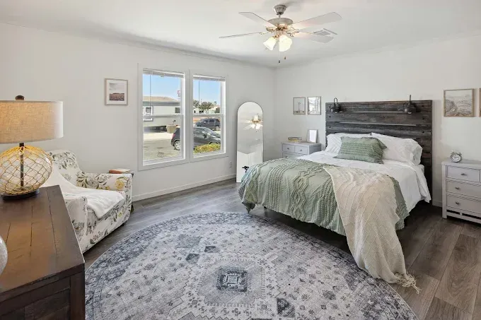 Bright bedroom with bed, chair, dresser, large windows, and gray patterned rug