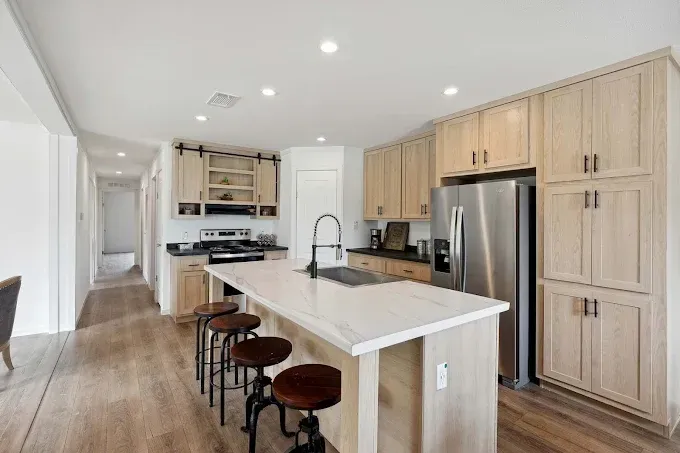 Bright modern kitchen with island, bar stools, light wood cabinets, and stainless steel appliances