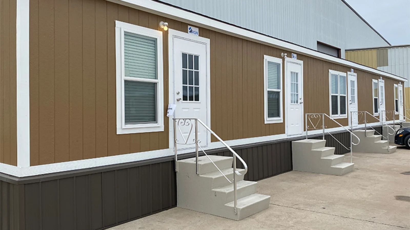 Row of brown and white modular buildings with white doors and small steps along a concrete walkway