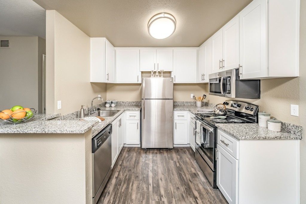 Modern white kitchen with granite counters and stainless-steel appliances.