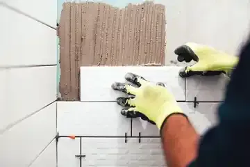 A man is installing tiles on a bathroom wall.