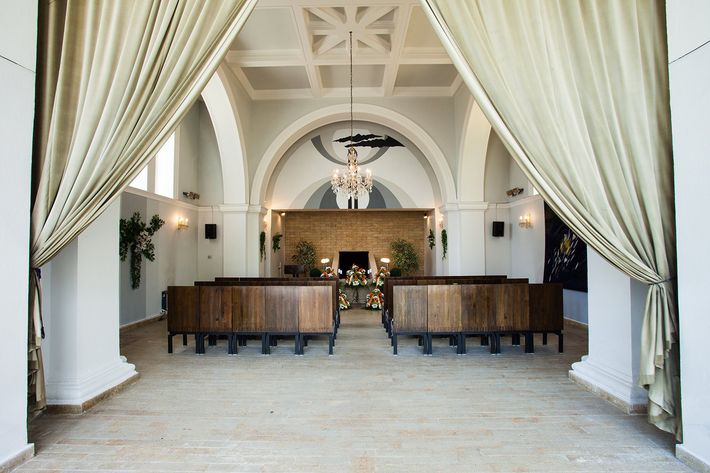Elegante ingresso con tende drappeggiate, lampadari e panche in legno sotto soffitti bianchi a volta.