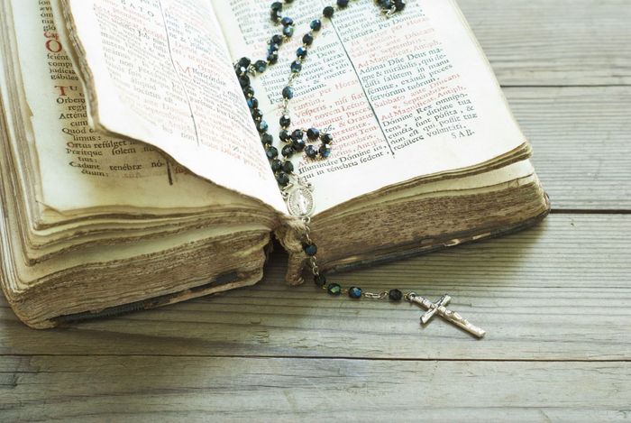 Bibbia aperta con rosario e crocifisso d'argento su un tavolo di legno