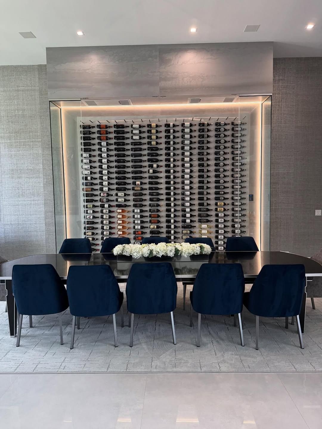 Formal dining room with blue chairs, long table, and a wine rack feature wall