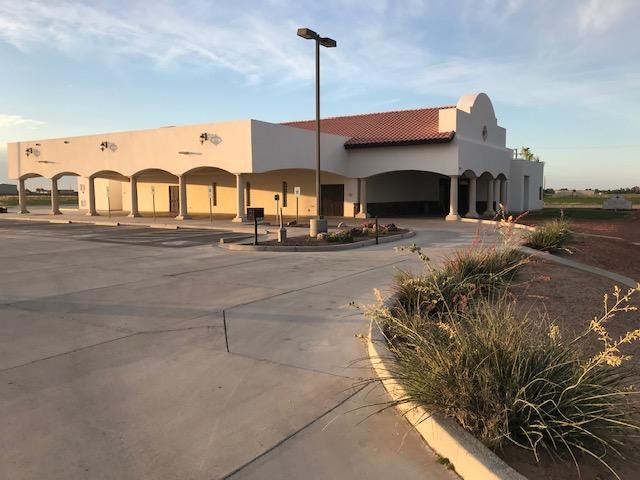 Empty storefront with arched facade and parking lot at sunset