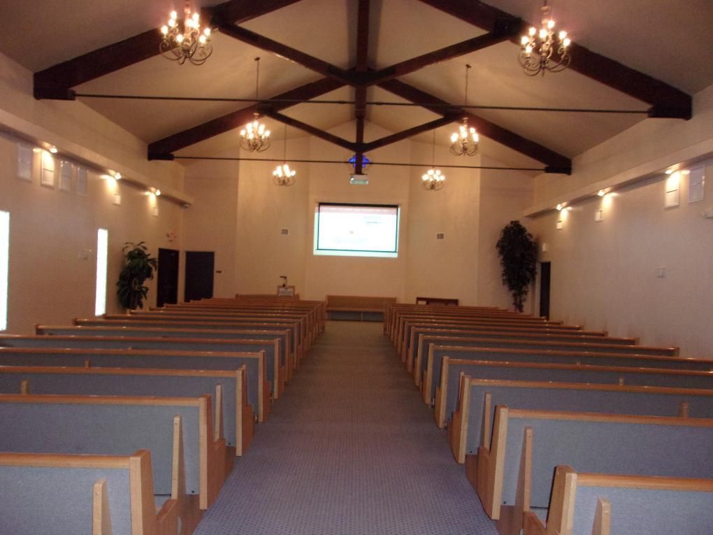 Empty church interior with rows of wooden pews, high ceiling, and a screen at the front