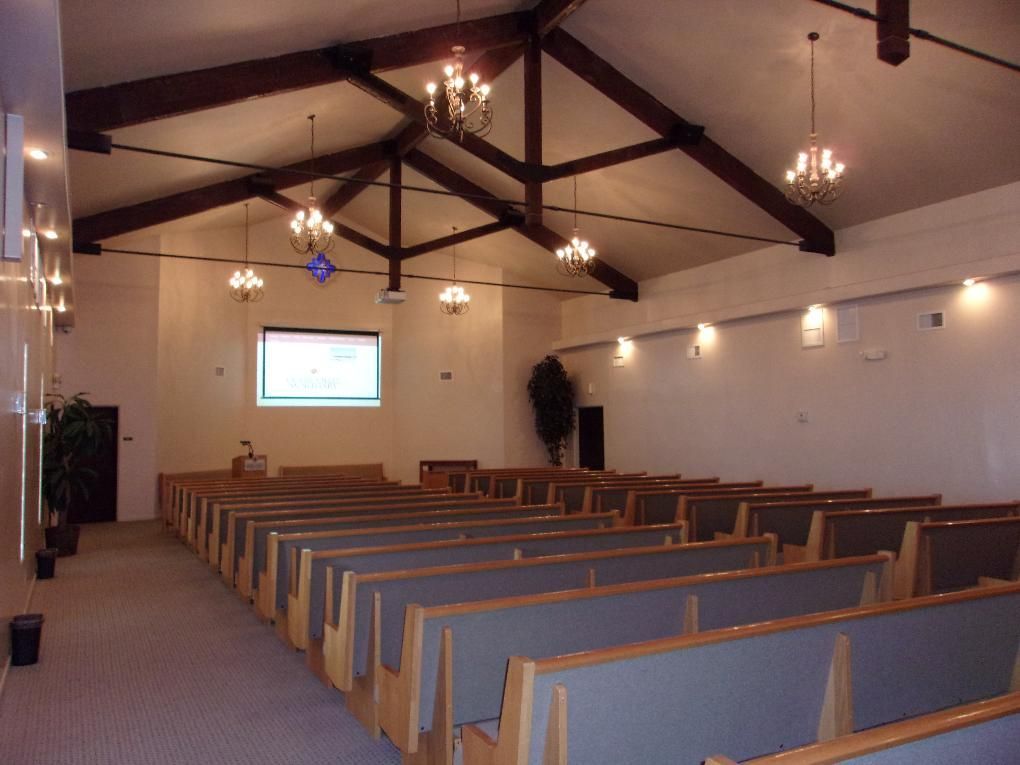 Empty church interior with rows of blue pews, wooden beams, and pendant lights