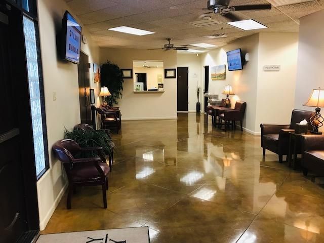 Empty lobby with polished floors, chairs, wall-mounted TVs, and a reception desk in the back.