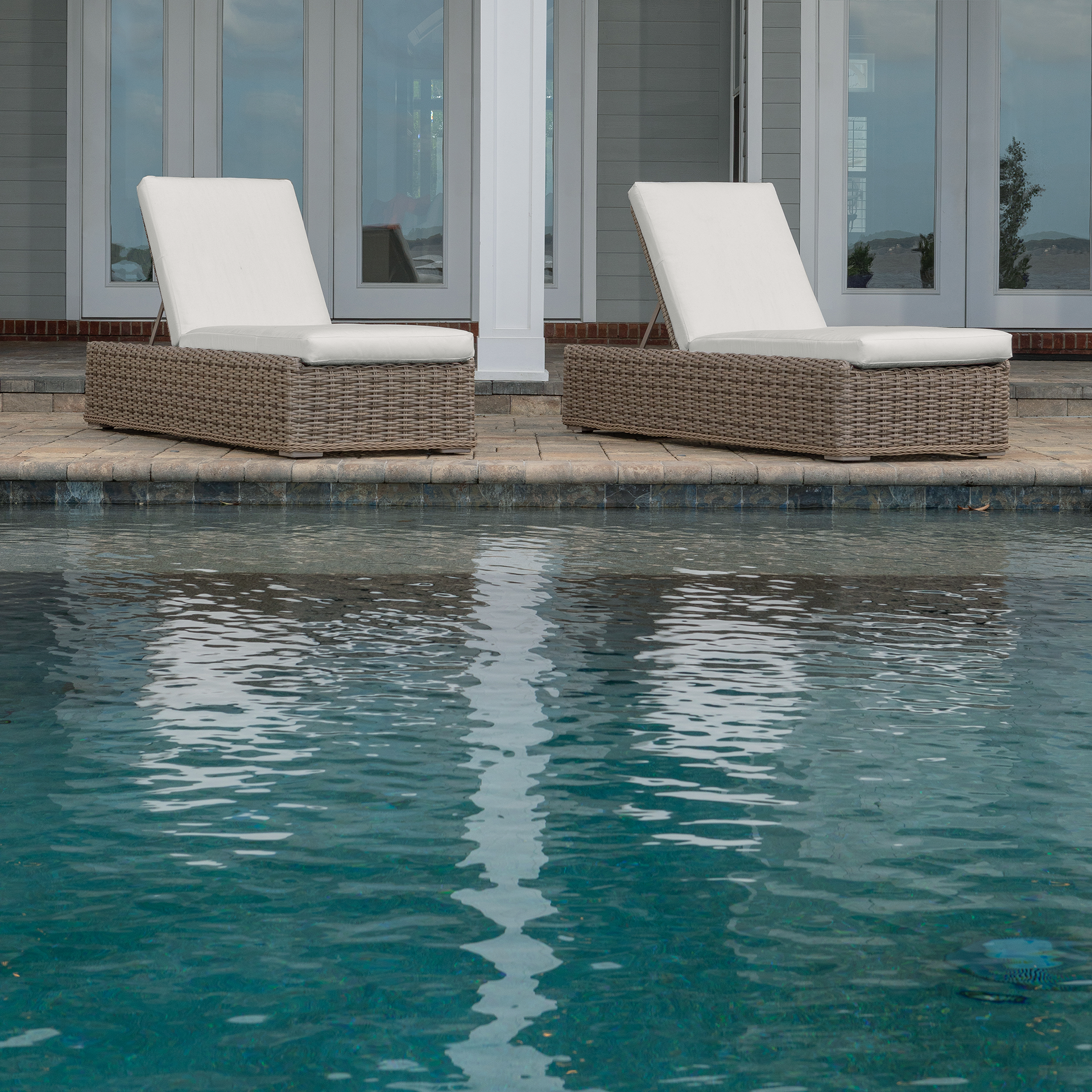 Two wicker chaise lounges by a pool, with white cushions.