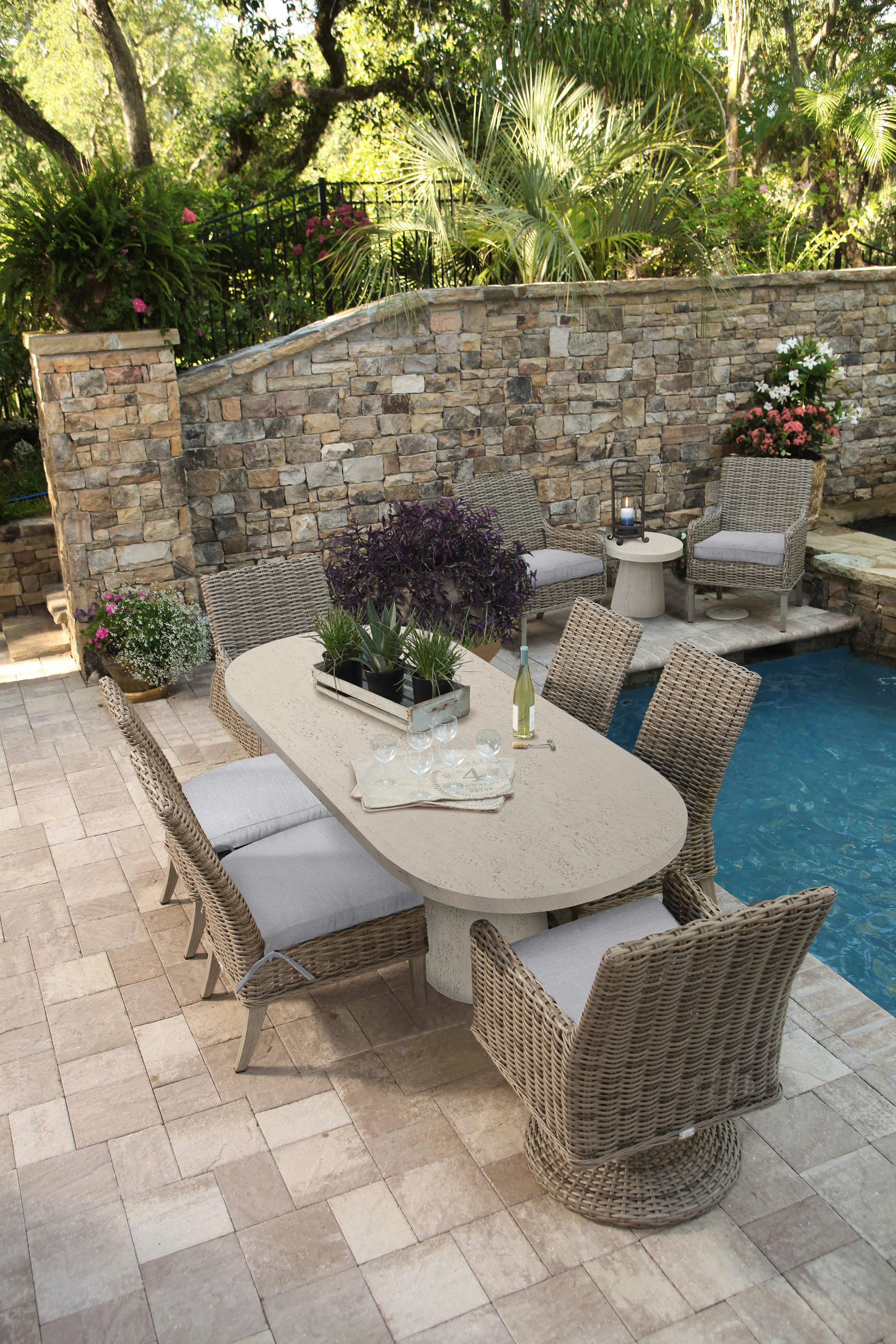 Patio dining set by a pool, featuring a stone wall and lush greenery.