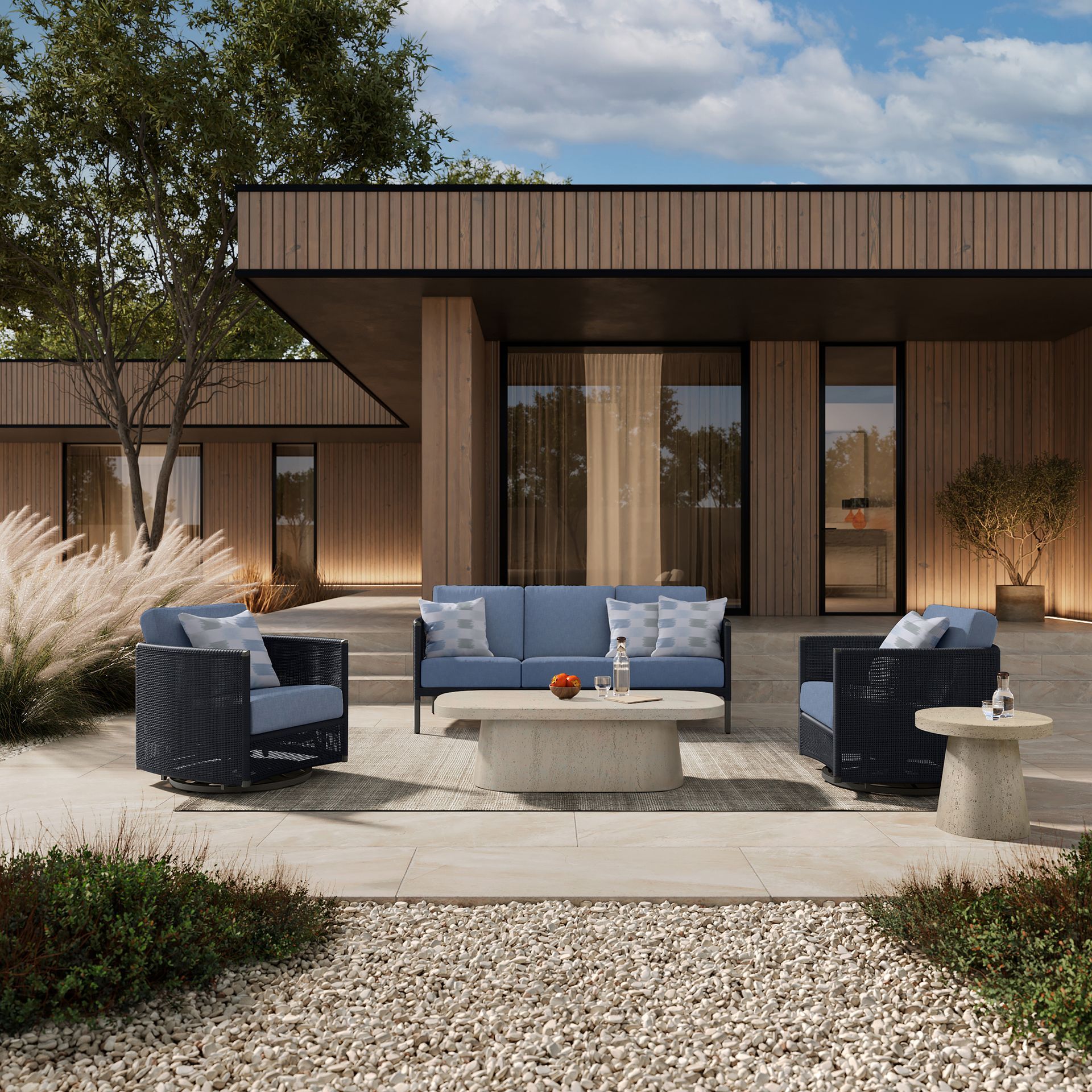 Outdoor patio set with blue cushions, stone table, and modern house in background.