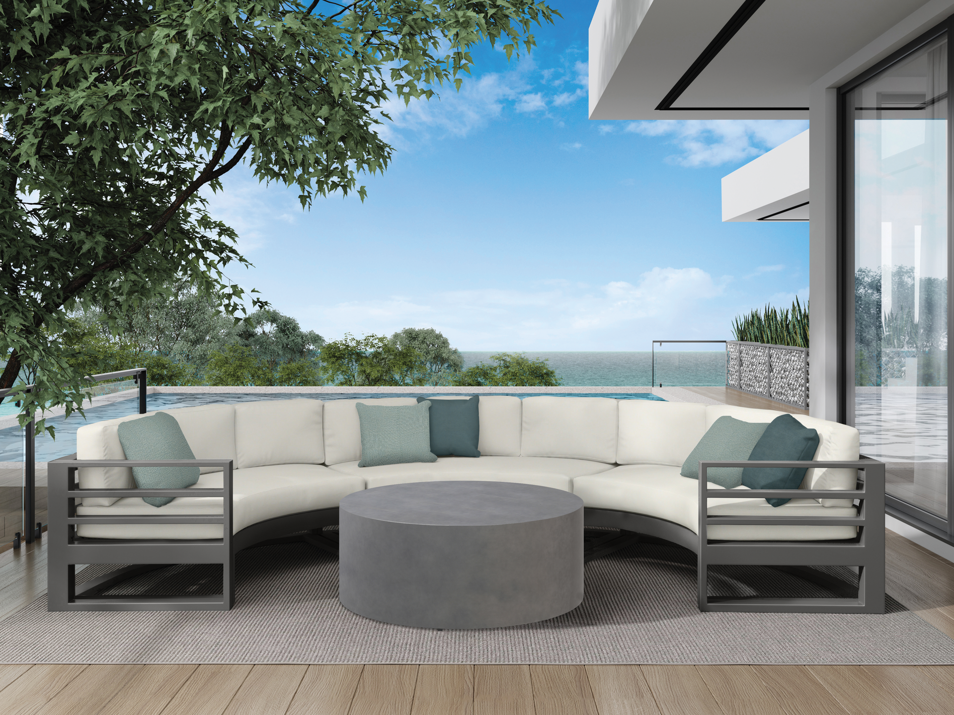 Outdoor curved sofa with gray frame and cushions, round coffee table, pool and ocean view.
