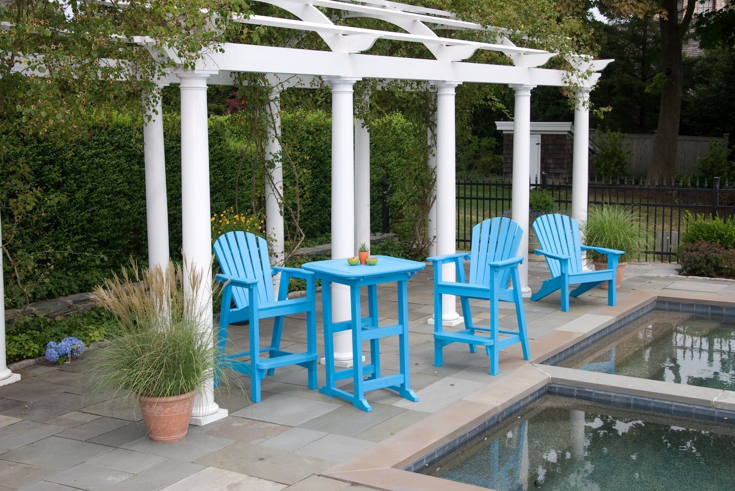 A patio with blue chairs and a table next to a pool.