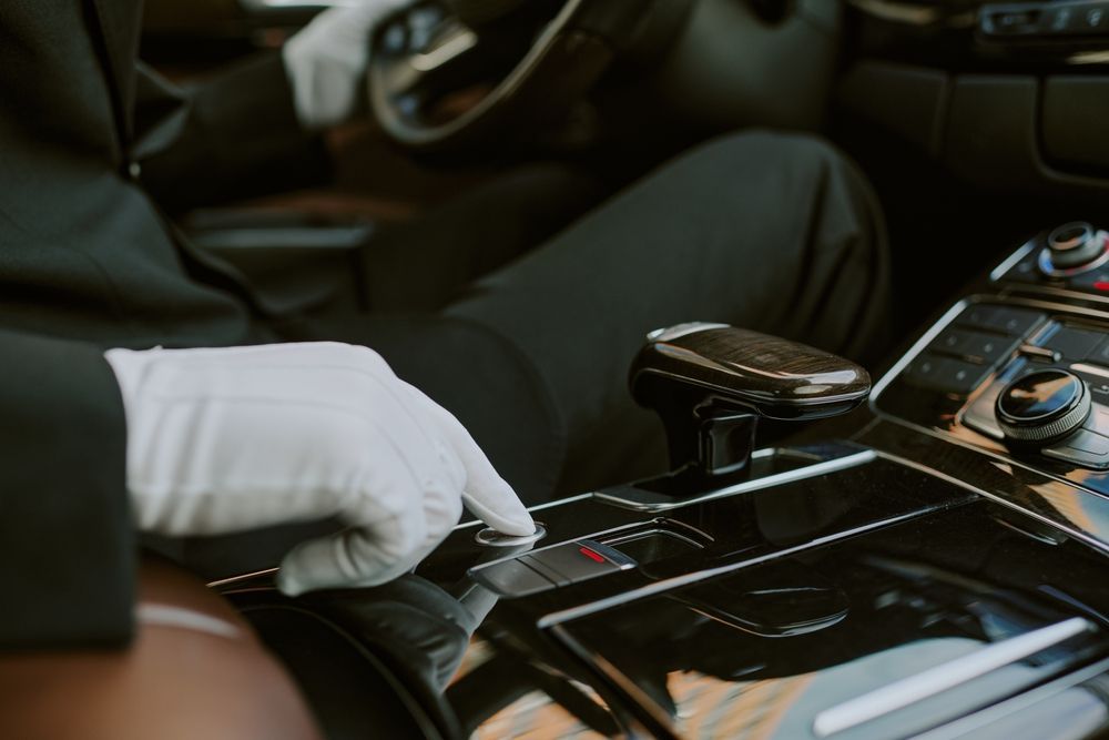 White-gloved hand shifts gear in a luxury car interior with a black center console and digital display.