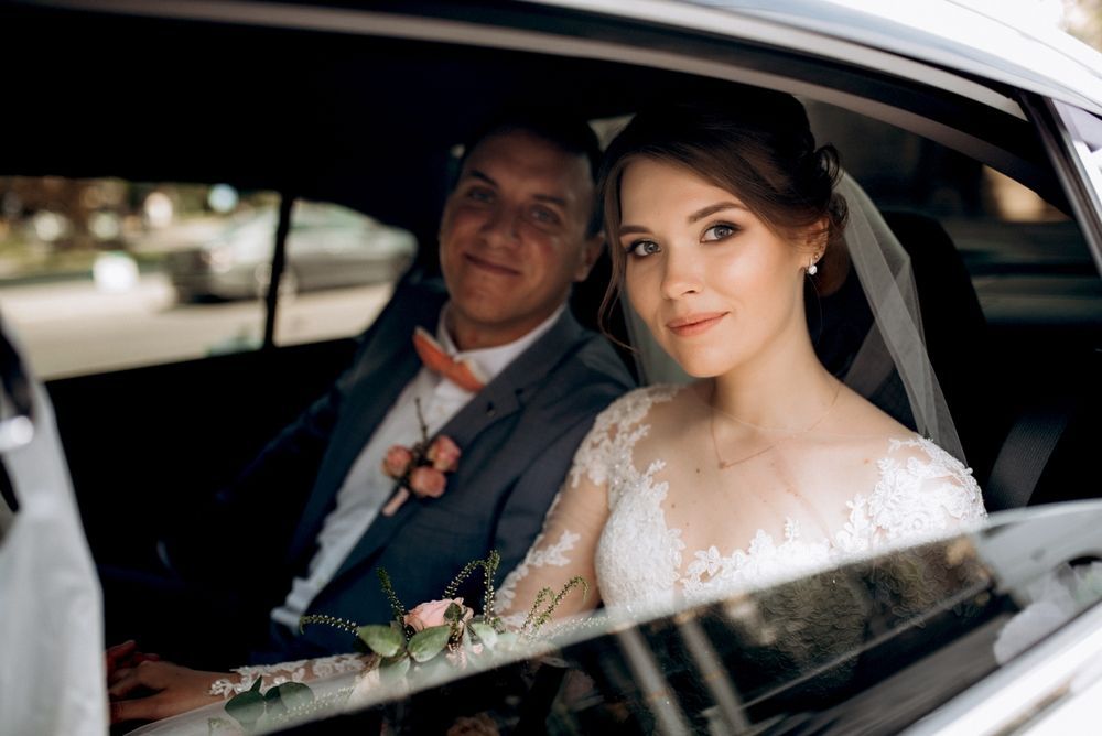 Bride and groom seated in a car, smiling through the window on their wedding day
